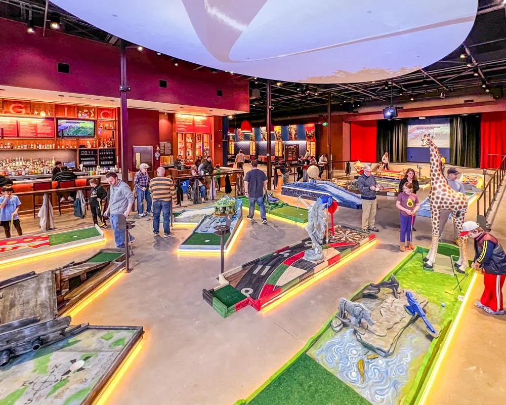 People playing indoor miniature golf. The holes are colorful and bright and lit up.