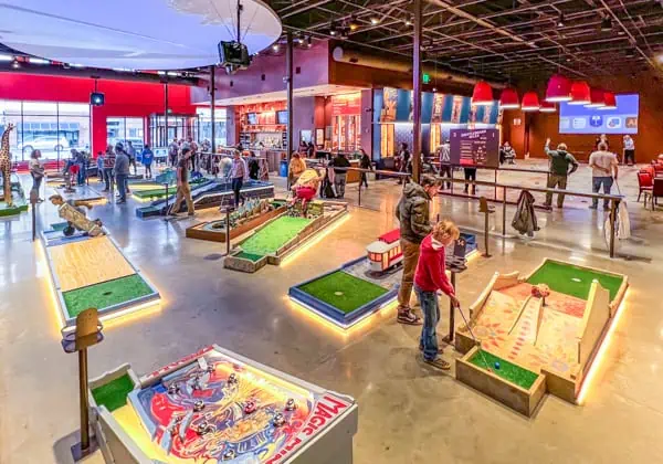 People playing indoor miniature golf. The holes are colorful and bright and lit up.